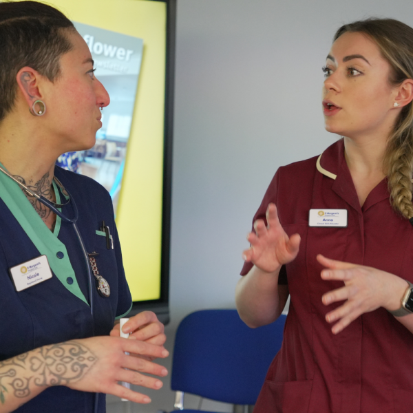 Two female clinicians talking to one another whilst gesturing.