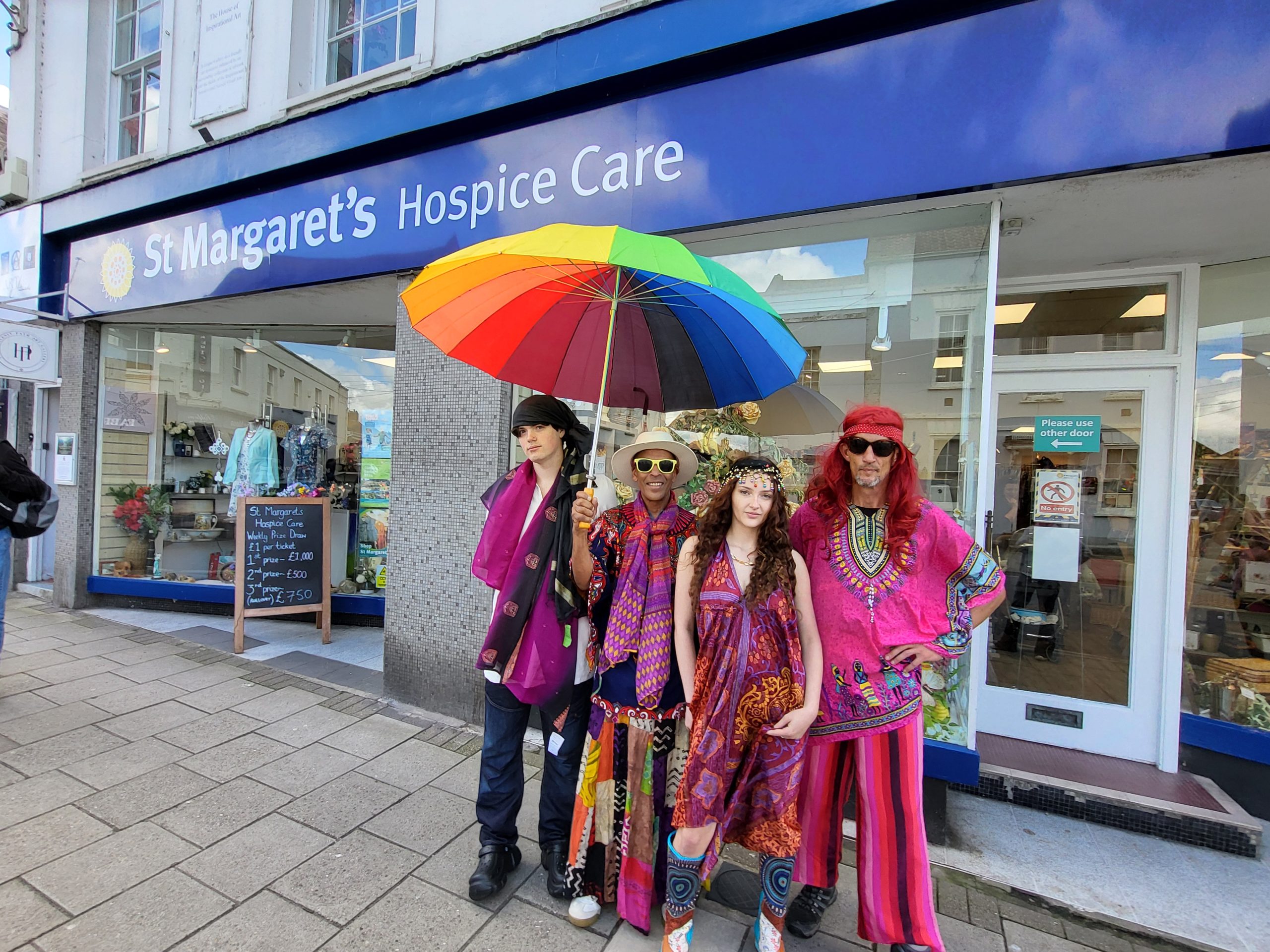 Four people in festival clothes stand outside St Margaret's Hospice shop in Glastonbury