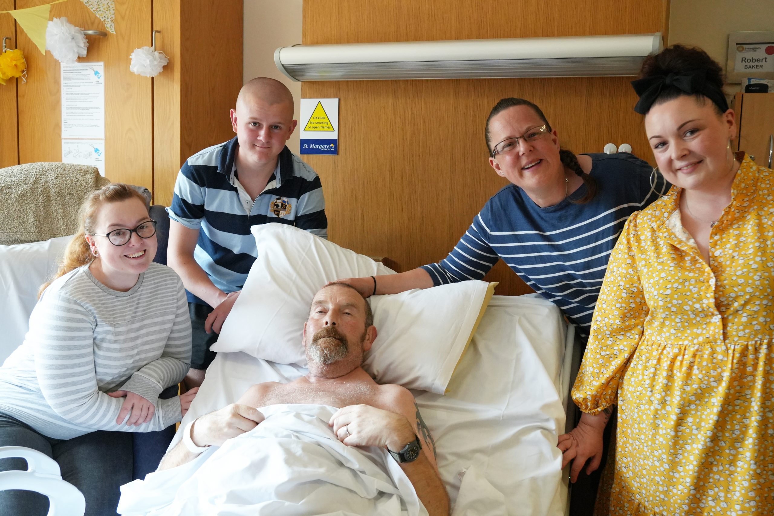 Family members stand around the bed - all smiling at camera