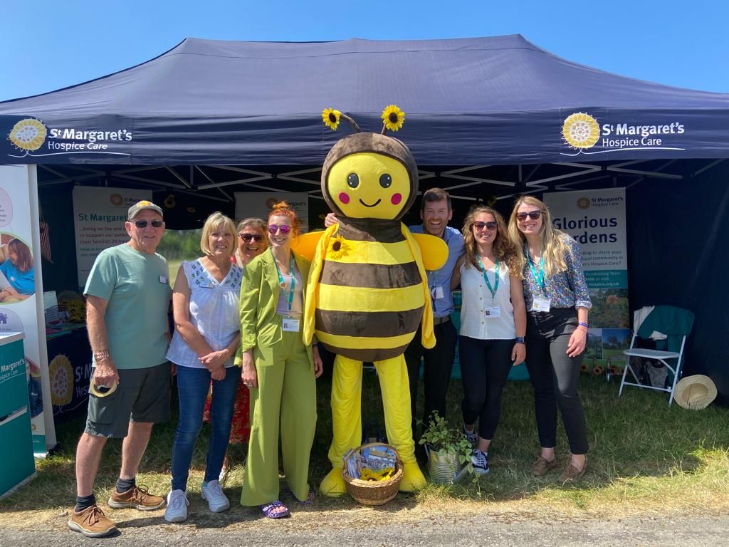 Group of people stood outside infront of a gazebo with a giant bee mascot