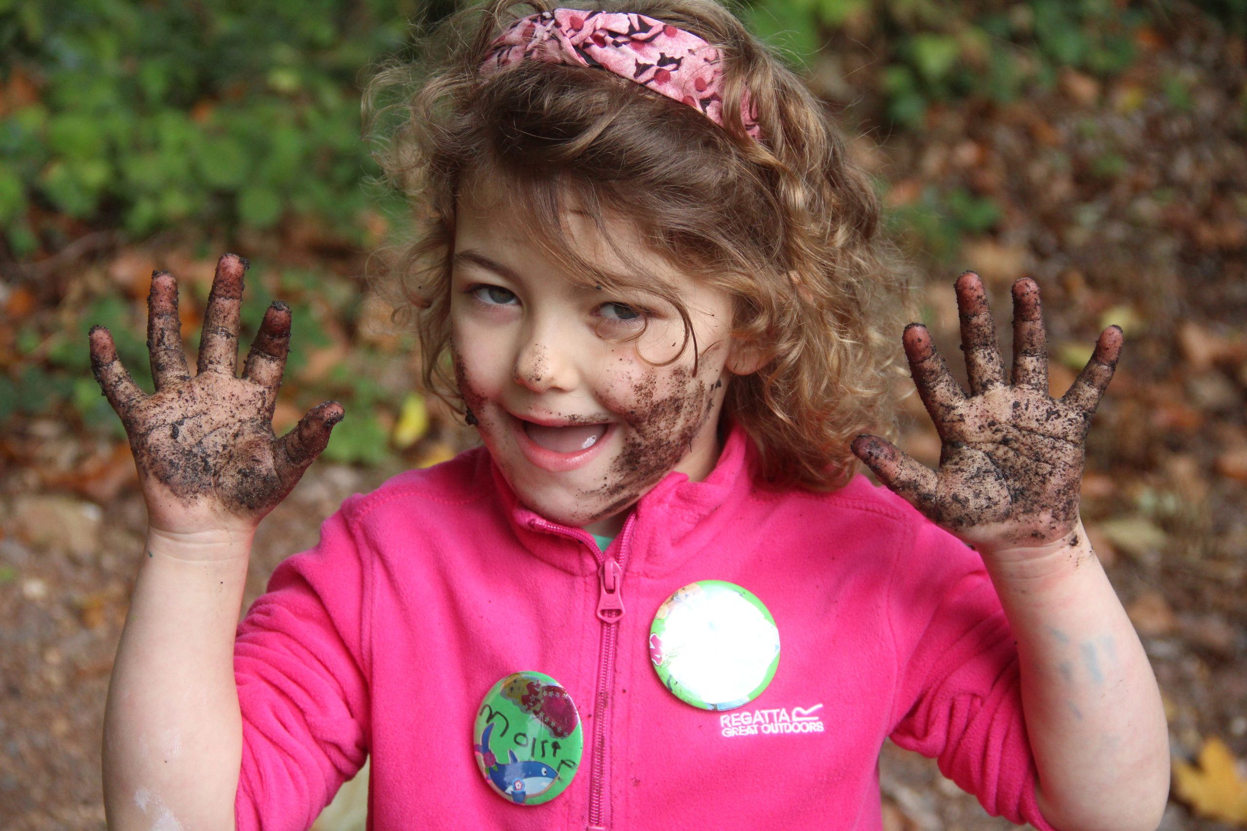 Little girl holds up her muddy hands to camera