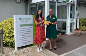 Two women standing outside Nuffield Health holding an envelope as part of St Margaret’s Hospice’s Charity £50 Challenge for businesses fundraising campaign.