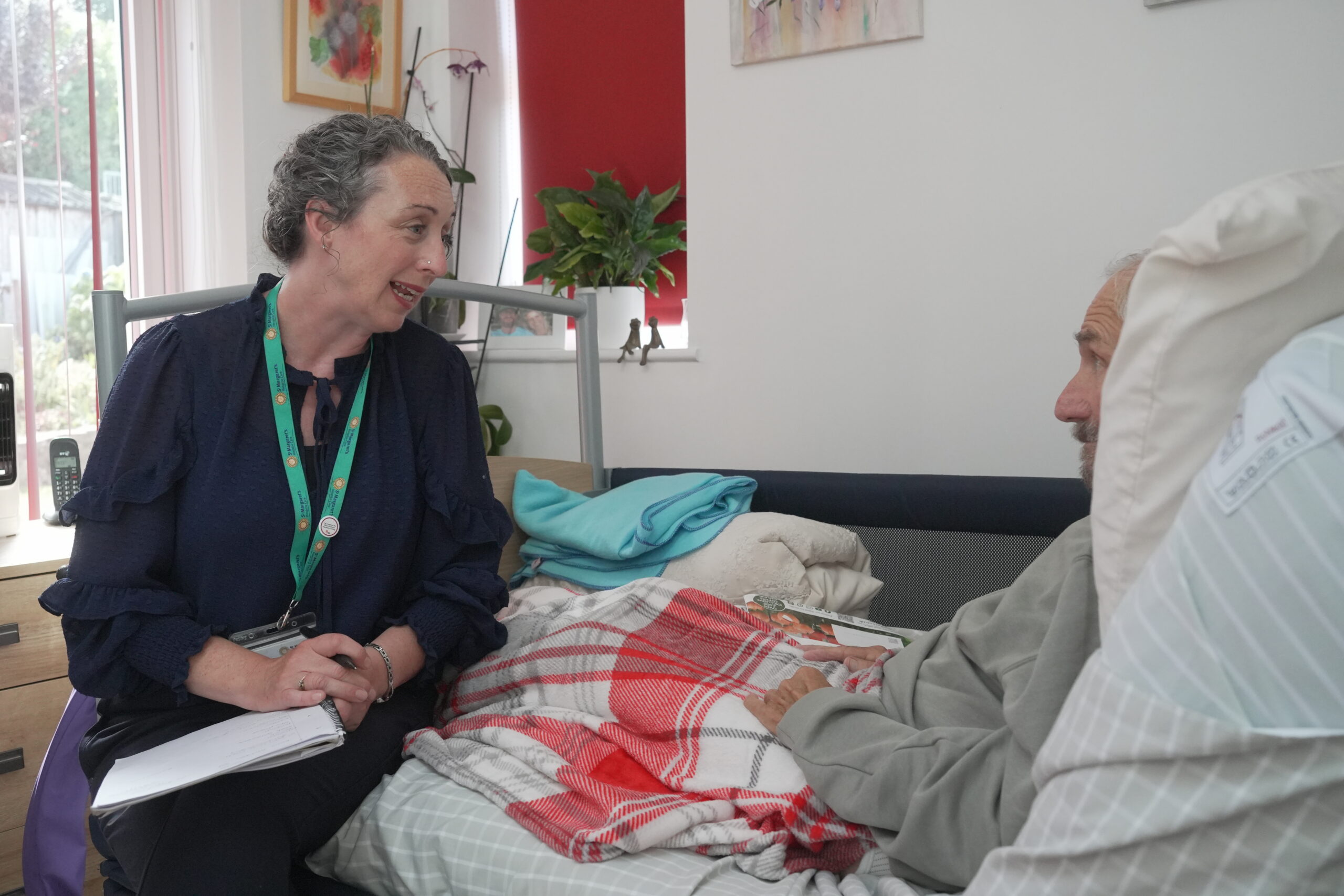 A community nurse speaking kindly to a patient who is being cared for in their own home.